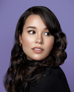 Model with black hair stands in front of a purple backdrop